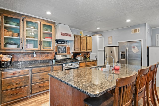 kitchen with sink, a textured ceiling, a kitchen bar, a kitchen island with sink, and appliances with stainless steel finishes