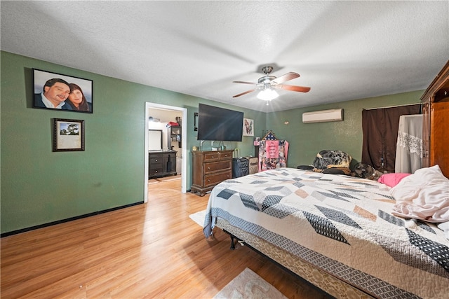 bedroom with a textured ceiling, ceiling fan, light hardwood / wood-style flooring, and a wall mounted air conditioner