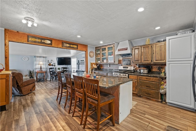 kitchen with light wood finished floors, a kitchen bar, gas range, and custom range hood