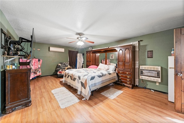 bedroom with a textured ceiling, heating unit, a wall mounted AC, ceiling fan, and light hardwood / wood-style floors