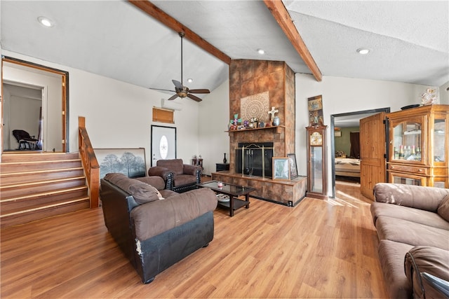 living room featuring a textured ceiling, a large fireplace, ceiling fan, beamed ceiling, and light hardwood / wood-style floors