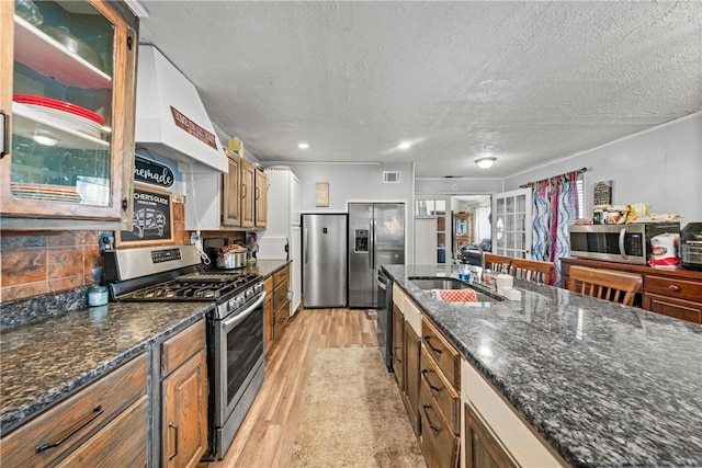 kitchen featuring custom range hood, a textured ceiling, stainless steel appliances, sink, and light hardwood / wood-style flooring