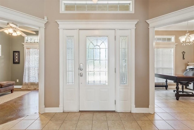 tiled foyer with a healthy amount of sunlight and ceiling fan with notable chandelier