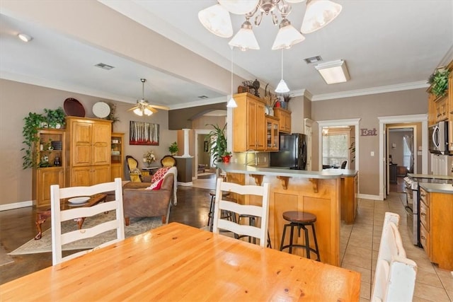 kitchen featuring a kitchen breakfast bar, kitchen peninsula, crown molding, light tile patterned floors, and appliances with stainless steel finishes