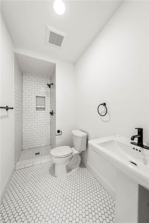 bathroom with a tile shower, toilet, and tile patterned floors