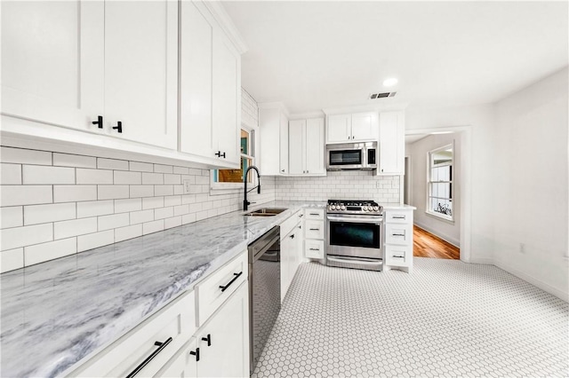 kitchen featuring light stone countertops, tasteful backsplash, stainless steel appliances, sink, and white cabinetry