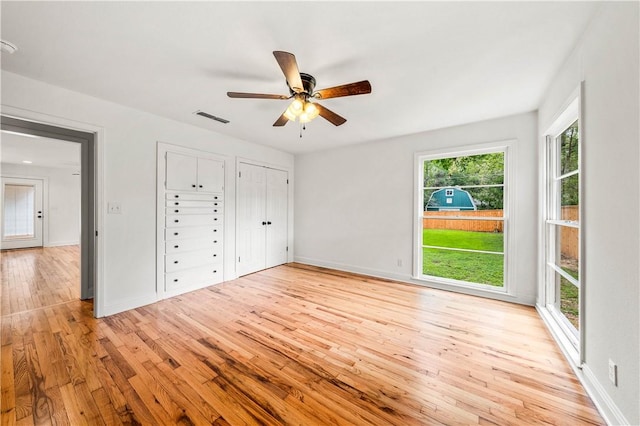 unfurnished bedroom featuring multiple closets, ceiling fan, and light hardwood / wood-style floors