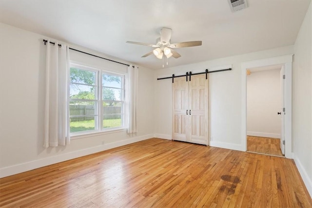 unfurnished bedroom with a barn door, ceiling fan, a closet, and light hardwood / wood-style floors