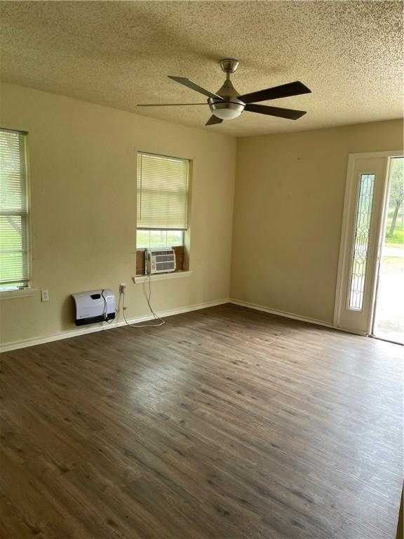 empty room with a textured ceiling, dark hardwood / wood-style flooring, a wealth of natural light, and ceiling fan