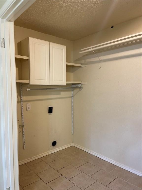 laundry area featuring electric dryer hookup, cabinets, light tile patterned floors, and a textured ceiling