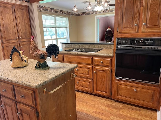 kitchen with light stone counters, light hardwood / wood-style flooring, a kitchen island, black appliances, and ornamental molding