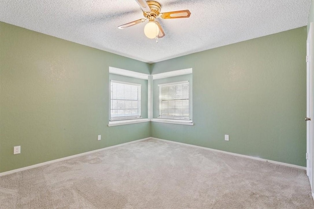 empty room with a textured ceiling, carpet floors, a ceiling fan, and baseboards