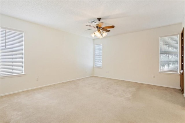 empty room featuring light carpet, a wealth of natural light, visible vents, and a textured ceiling