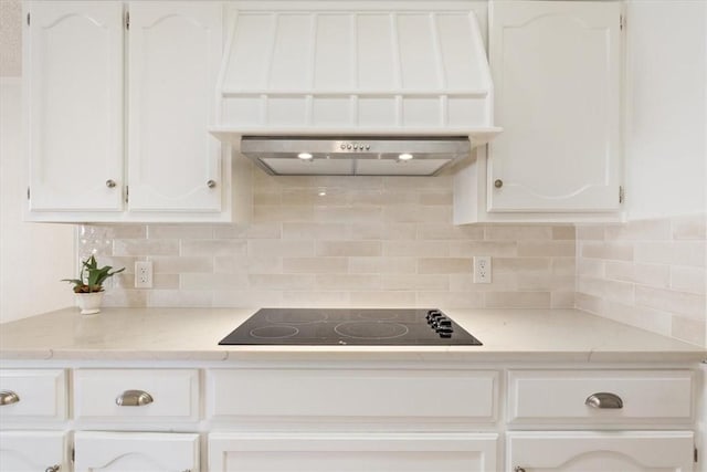 kitchen featuring decorative backsplash, white cabinetry, custom exhaust hood, and black electric stovetop