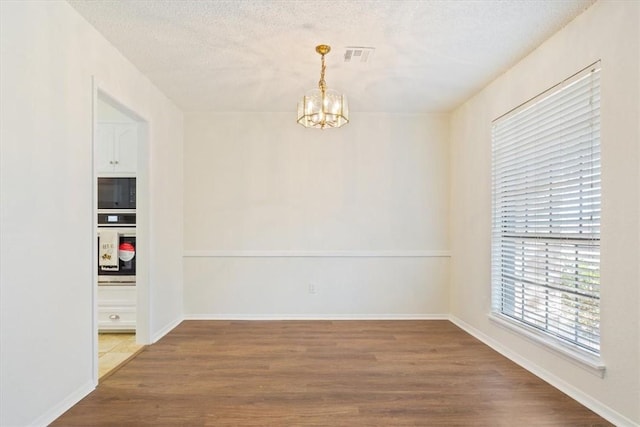 unfurnished room featuring a textured ceiling, a notable chandelier, wood finished floors, visible vents, and baseboards