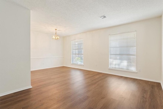 empty room featuring a notable chandelier, a textured ceiling, and wood finished floors