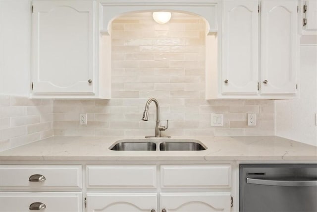 kitchen with backsplash, light stone countertops, stainless steel dishwasher, white cabinetry, and a sink