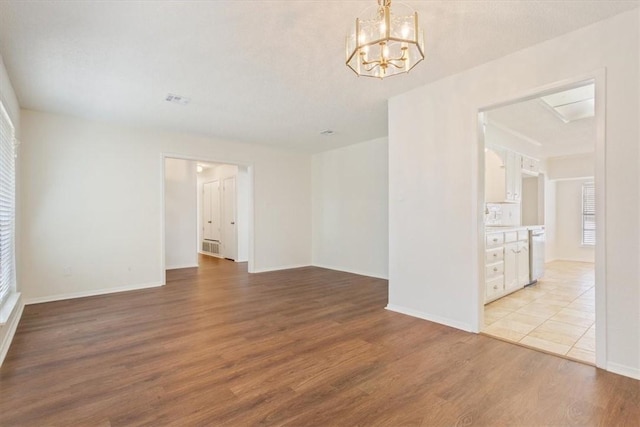 empty room with a chandelier, baseboards, visible vents, and light wood finished floors