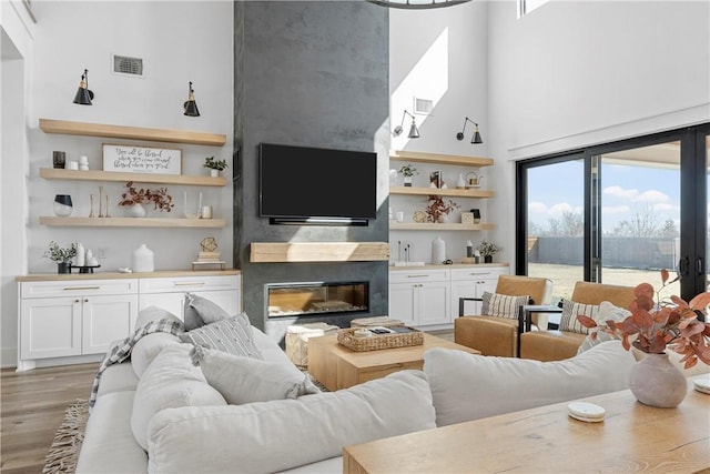 living room featuring a high ceiling, hardwood / wood-style floors, a high end fireplace, and built in shelves