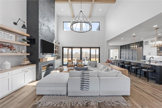 living room with beam ceiling, a high end fireplace, an inviting chandelier, and light hardwood / wood-style flooring