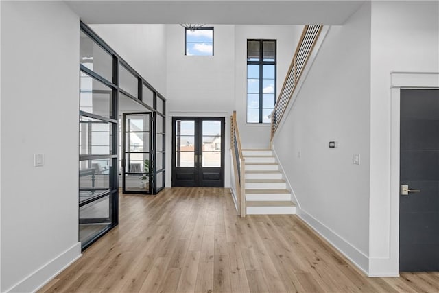 entryway with a towering ceiling, a healthy amount of sunlight, light wood-type flooring, and french doors