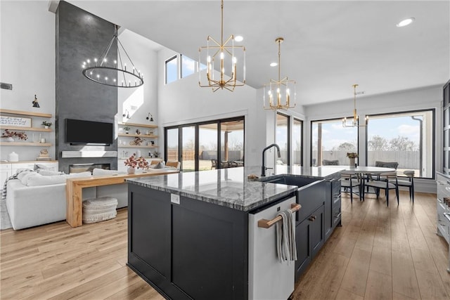 kitchen with an island with sink, hanging light fixtures, stainless steel dishwasher, light hardwood / wood-style floors, and an inviting chandelier