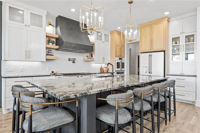 kitchen featuring stainless steel appliances, an island with sink, custom range hood, and an inviting chandelier