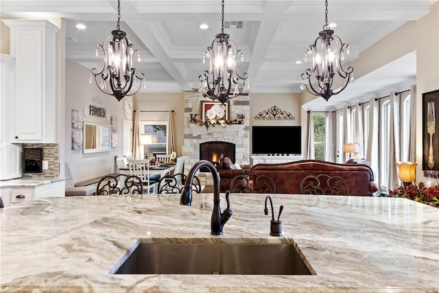 kitchen featuring a stone fireplace, sink, ornamental molding, decorative light fixtures, and beam ceiling