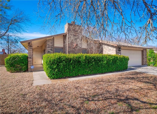 mid-century home featuring brick siding, fence, concrete driveway, a chimney, and an attached garage