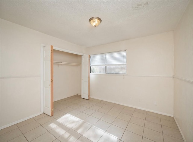 unfurnished bedroom featuring light tile patterned flooring, baseboards, a closet, and a textured ceiling