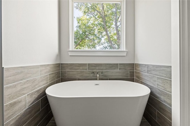 bathroom with a tub to relax in and tile walls