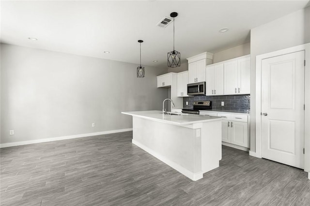 kitchen with white cabinetry, stainless steel appliances, hardwood / wood-style floors, pendant lighting, and a kitchen island with sink