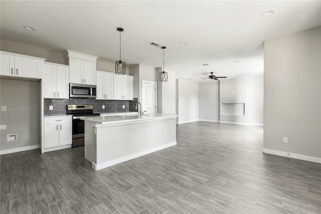 kitchen featuring appliances with stainless steel finishes, a kitchen island with sink, ceiling fan, white cabinetry, and hanging light fixtures