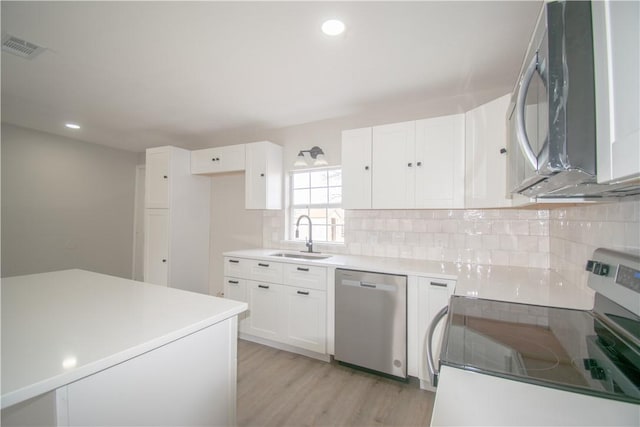 kitchen featuring light wood finished floors, tasteful backsplash, white cabinets, stainless steel appliances, and a sink