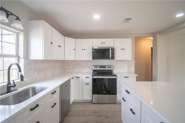 kitchen with appliances with stainless steel finishes, white cabinetry, a sink, and backsplash