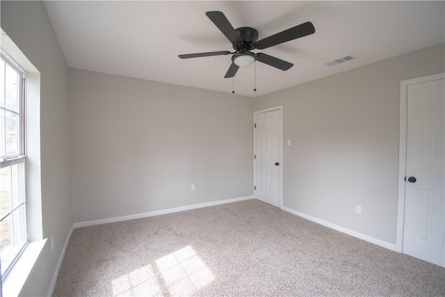 carpeted empty room with visible vents, ceiling fan, and baseboards