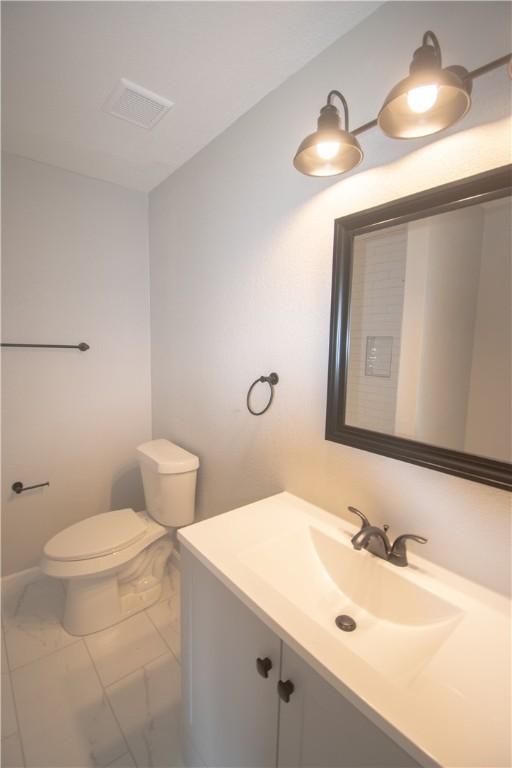 half bathroom with marble finish floor, visible vents, vanity, and toilet