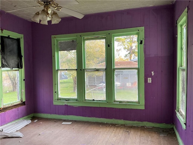 unfurnished room featuring ceiling fan, wooden walls, and hardwood / wood-style flooring