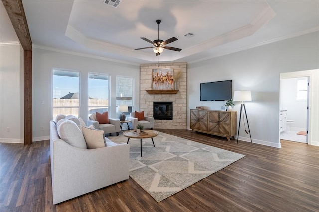 living room with ceiling fan, a fireplace, dark hardwood / wood-style floors, a raised ceiling, and ornamental molding