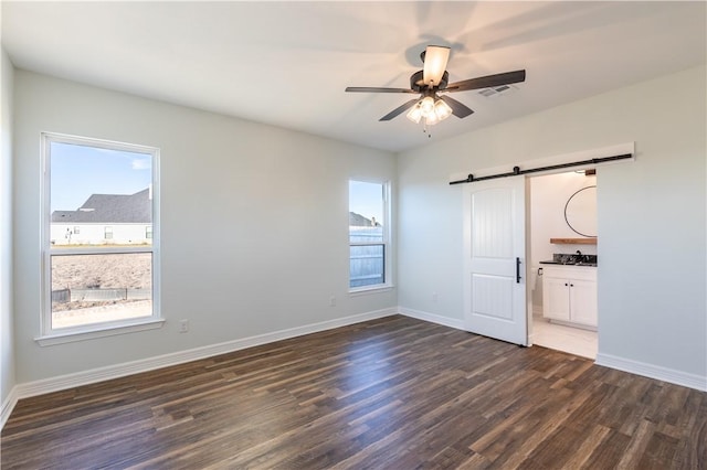 unfurnished bedroom featuring ceiling fan, multiple windows, dark hardwood / wood-style flooring, and a barn door