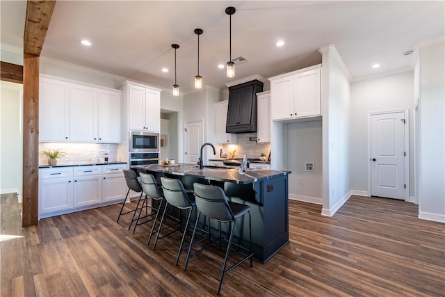 kitchen with decorative light fixtures, white cabinetry, a center island with sink, and built in microwave