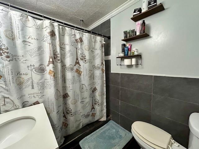 bathroom featuring sink, toilet, ornamental molding, tile walls, and walk in shower