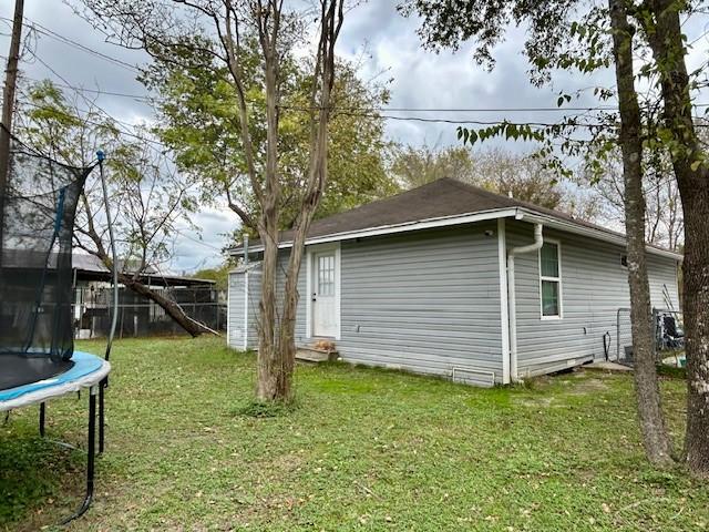 rear view of property with a yard and a trampoline