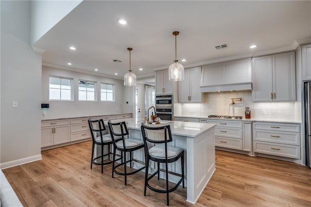 kitchen with white cabinetry, an island with sink, hanging light fixtures, and light hardwood / wood-style flooring