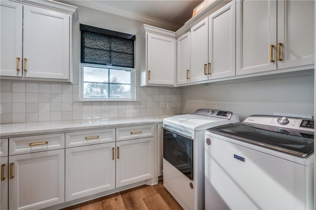 washroom with cabinets, light wood-type flooring, washing machine and dryer, and ornamental molding