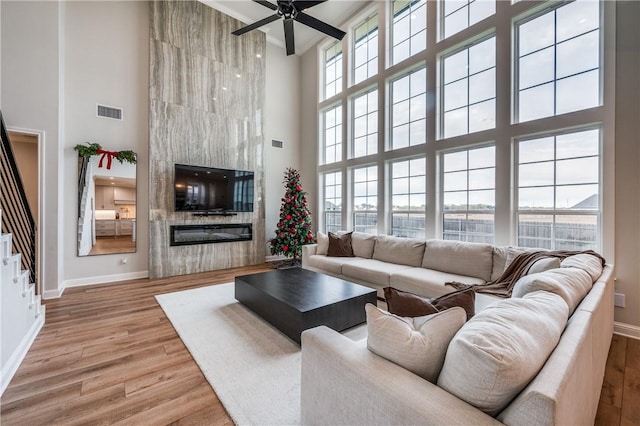 living room with a fireplace, ceiling fan, hardwood / wood-style floors, and a high ceiling