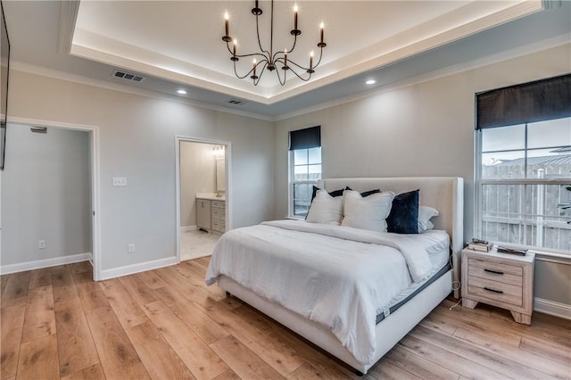 bedroom featuring connected bathroom, light hardwood / wood-style floors, crown molding, and a tray ceiling