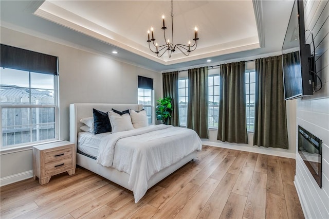 bedroom with an inviting chandelier, light wood-type flooring, ornamental molding, and a tray ceiling