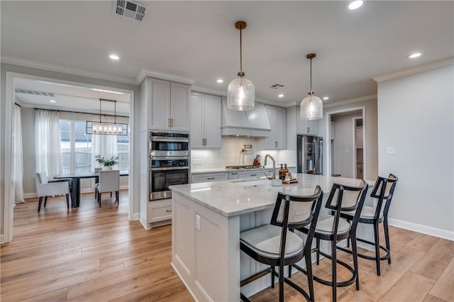 kitchen featuring a large island with sink, sink, light wood-type flooring, a breakfast bar area, and stainless steel appliances