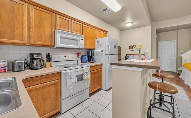 kitchen featuring white appliances, visible vents, a kitchen island, a breakfast bar, and a sink